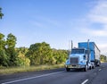 Blue day cab classic big rig semi truck transporting cargo in blue semi trailer moving on the straight highway at sunny day Royalty Free Stock Photo