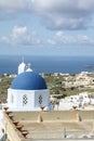 The blue-domed church in Santorini surrounded by buildings and the sea at daytime in Greece Royalty Free Stock Photo