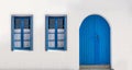 Blue door and two windows with open shutters on white wall. Greek island house front view Royalty Free Stock Photo