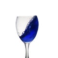 A blue drink is poured into wine glass causing a splash, isolated on white background Royalty Free Stock Photo