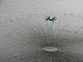 A blue drone flying over a lake forming a rippled surface on the water no one horizontal