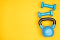 Blue dumbbells and a kettlebell on yellow background