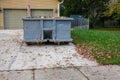 A blue dumpster filled with construction debris in the driveway of a yellow house in front of the garage doors Royalty Free Stock Photo