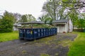 Blue dumpster filled with vegetation debris is seen in the driveway of a house being renovated