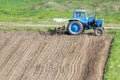 Blue dusty tractor with seedbed cultivator standing at the edge of freshly plowed and cultivated field, soil prepared for sowing. Royalty Free Stock Photo