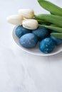 Blue dyed Easter eggs and white tulip flowers bouquet on plate on white neutral marble table background, aesthetic Royalty Free Stock Photo