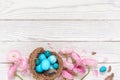 Blue easter eggs in bird`s nest with ranunculus flowers on white wooden background. Spring concept. Top view, copy space Royalty Free Stock Photo