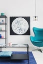 Blue egg chair in bright living room with black metal furniture and moon graphic on the wall, real photo Royalty Free Stock Photo