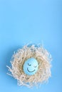 Blue egg with painted smiles in the nest, copy space. Happy Easter concept greeting card design