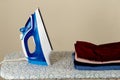 Blue electric iron and pile of clothes on ironing board Royalty Free Stock Photo