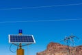 Blue emergency light fixture powered by solar panel. Blurred transmission tower background