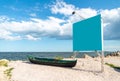 Blue empty billboard next to a local, wooden fishing boat, on the sand, at shore of the Black Sea Marea Neagra, Romanian coast.