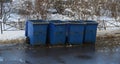 Blue empty plastic mobile garbage containers stand on the asphalt near a snow-covered lawn Royalty Free Stock Photo