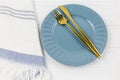 Blue empty plate with fork, knife, white striped textile napkins on wooden table. Golden cutlery, table setting utensils Royalty Free Stock Photo