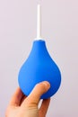 Blue enema in a hand on white background for flushing the intestines with constipation