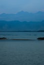 Blue evening on sea with mountains in fog on horizon in calm cloudy sunset, vertical. Overcast landscape on indonesian island. Royalty Free Stock Photo