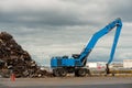 Blue excavator with claw arm in a scrap metal yard. Metal recycling industry. Export of junk for profit and ecology. Port area Royalty Free Stock Photo