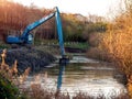 Blue excavator cleaning river in a park, Warm morning light