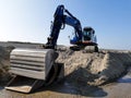 Blue excavator on pile of sand in muddy sand