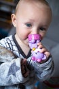 Baby girl in grey clothes and bathrobe holds in hands and nibble a violet toy cat. First tooth. Closeup portrait of blue Royalty Free Stock Photo