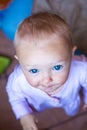 Blue eye blond baby portrait. Child in pink shirt looks straight up to the camera. Blanket and toys in background, kid