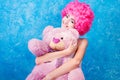 Blue eye comic girl / woman / teenager with pink curly wig is hugging teddy bear Royalty Free Stock Photo