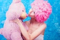 Blue eye comic girl / woman / teenager with pink curly wig is kissing teddy bear Royalty Free Stock Photo