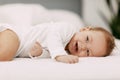 A blue-eyed baby lies in a snow-white bed under a blanket, laughs and indulges Royalty Free Stock Photo