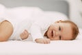 A blue-eyed baby lies in a snow-white bed under a blanket, laughs and indulges Royalty Free Stock Photo