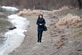 Blue-eyed beautiful woman with red curly hair walks on river in winter or late autumn Royalty Free Stock Photo