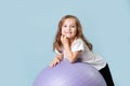 blue-eyed curly toddler girl laughs playing on lilac fitness ball.