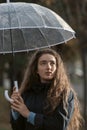 Blue-eyed girl with wavy hair looks wistfully to side holding transparent umbrella in hands. Vertical frame Royalty Free Stock Photo