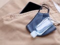 Blue fabric face mask with alcohol bottle gel and smartphone in pocket brown long pants.