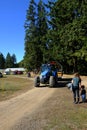 Blue farm tractor with big green trees on a dirt road with blue sky