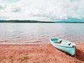 Blue fishing boat anchored on beach sand of lake. Smooth level