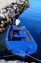 Blue fishing boat with covered motor tied to concrete molo, boarding platform on stony molo in background