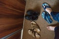 Blue flip flops and feet in an entrance of the home. black Shoes and brown old fashioned carpet. Wood door for wardrobe