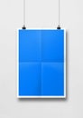 Blue folded poster hanging on a white wall with clips