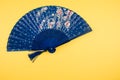 Blue folding hand fan isolated on a yellow background with free space for text Royalty Free Stock Photo