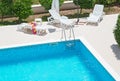 Blue fresh swimming pool with ladder stainless handrails stairs into the water, chairs for tanning and green plants. Royalty Free Stock Photo