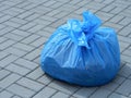 Blue garbage bag full of trash standing on the gray stone paving slabs Royalty Free Stock Photo