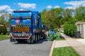 A blue garbage truck collects trash from large garbage bins on the side of a residential street