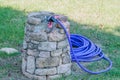 Blue garden hose coiled beside stone water tap Royalty Free Stock Photo