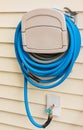 Blue gardening hose hanging on the house wall. Garden hose hangout, wall hose reel Royalty Free Stock Photo
