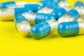 Blue gelatin capsules with white granules inside, isolated on a yellow background, macro shot. Royalty Free Stock Photo