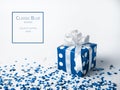 Blue gift box with bow on white background with confetti. The color of 2020 is classic blue