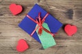 Blue gift box with red ribbon, blank gift tag and and red hearts on wooden background. Royalty Free Stock Photo