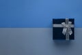 Blue gift box with silver bow on two-tone monochrome trendy classic blue paper background top view with copy space. Royalty Free Stock Photo