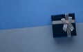 Blue gift box with silver bow on two-tone monochrome trendy classic blue paper background top view with copy space. Royalty Free Stock Photo