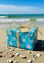 A blue gift box with a starfish and fish pattern is set on a sandy beach. The box is tied Royalty Free Stock Photo
